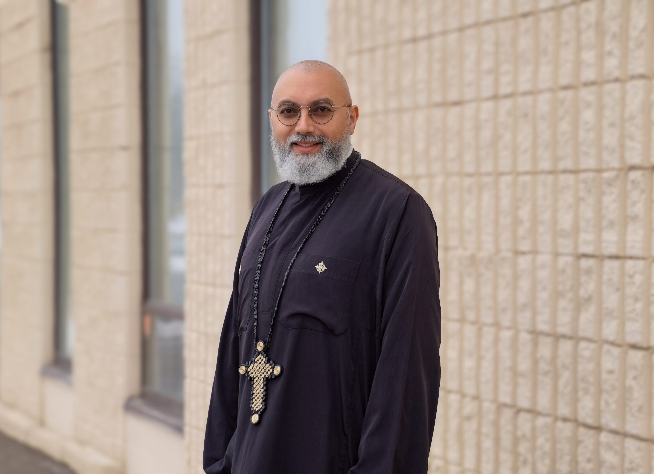 Father Pishoy standing outside the Cornerstone building smiling while looking at the camera