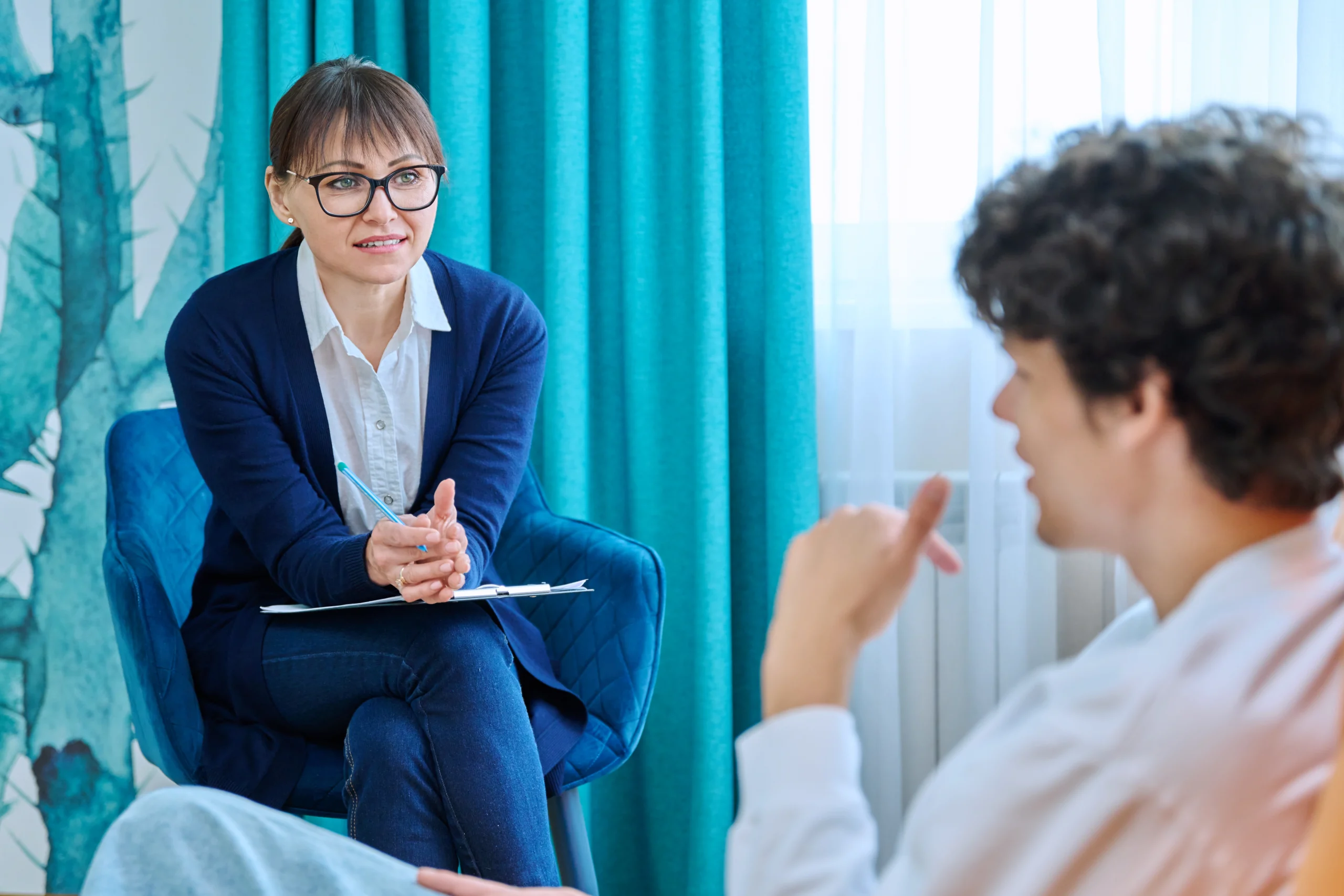 A female therapist with a clip board and a pen looking intently at a male intern