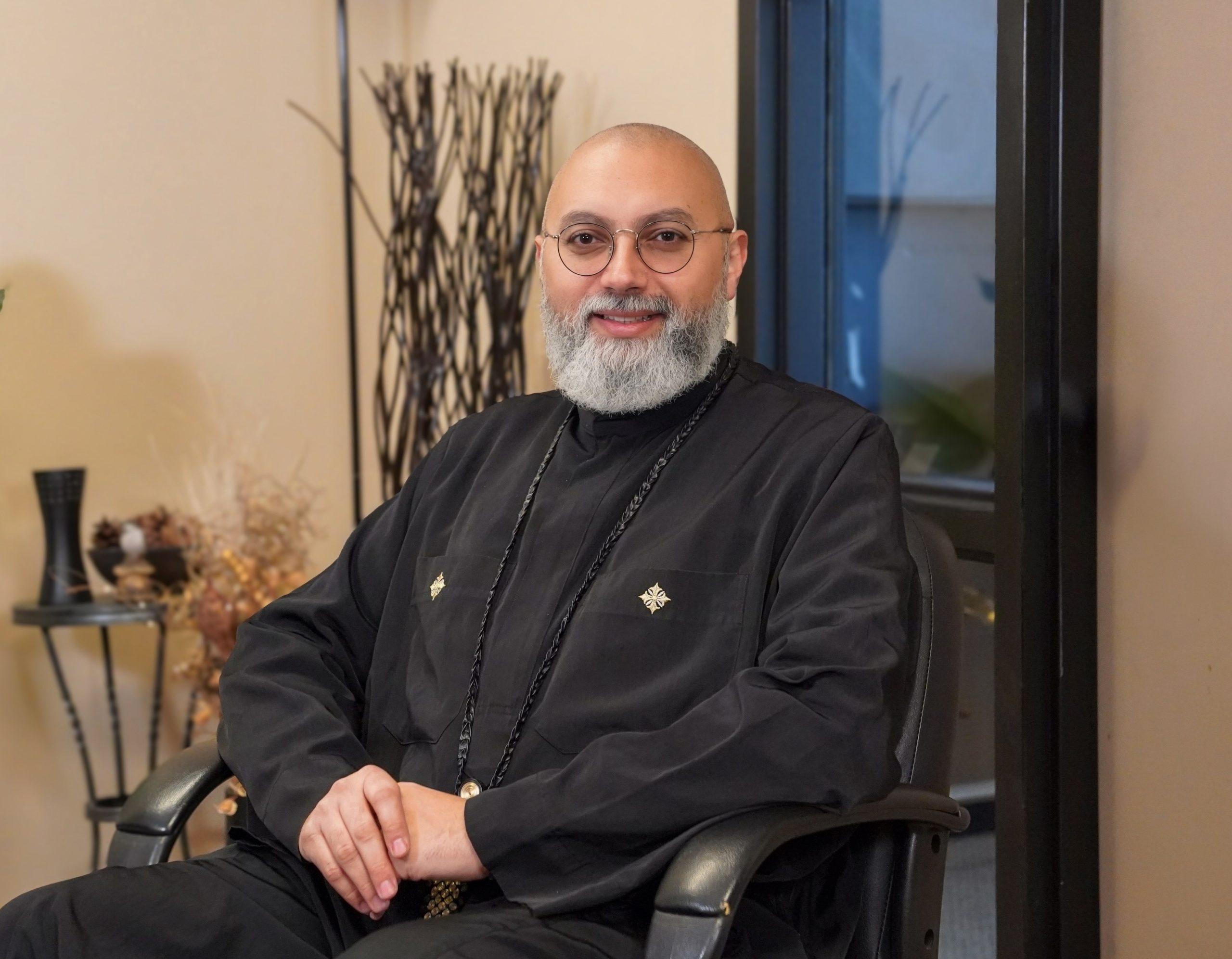 Father Pishoy Wafsy sitting in a chair smiling at the camera