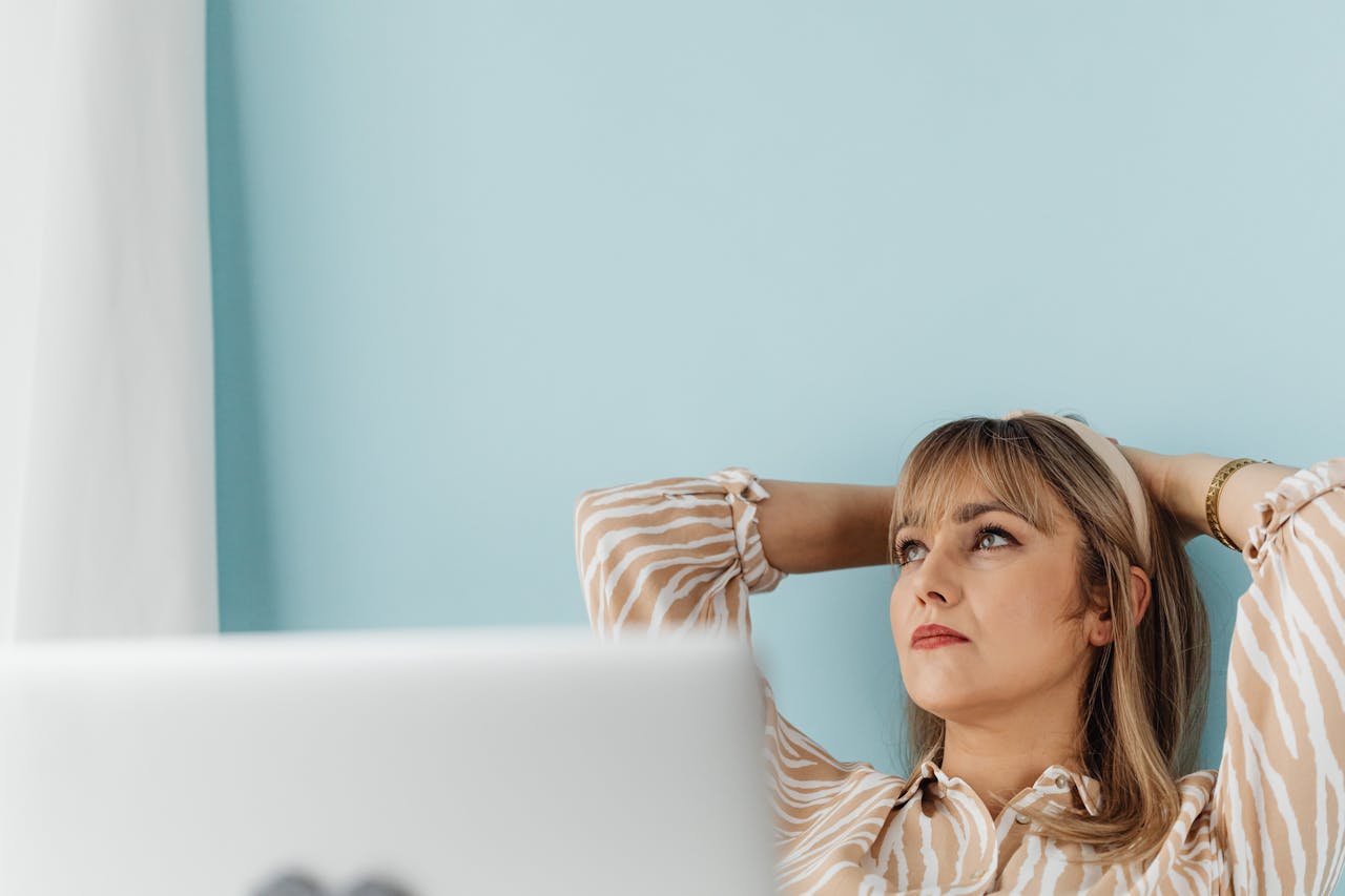 Blonde woman sitting by a laptop thinking
