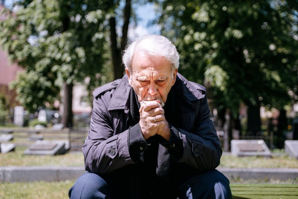 Older man grieving sitting on a park bench