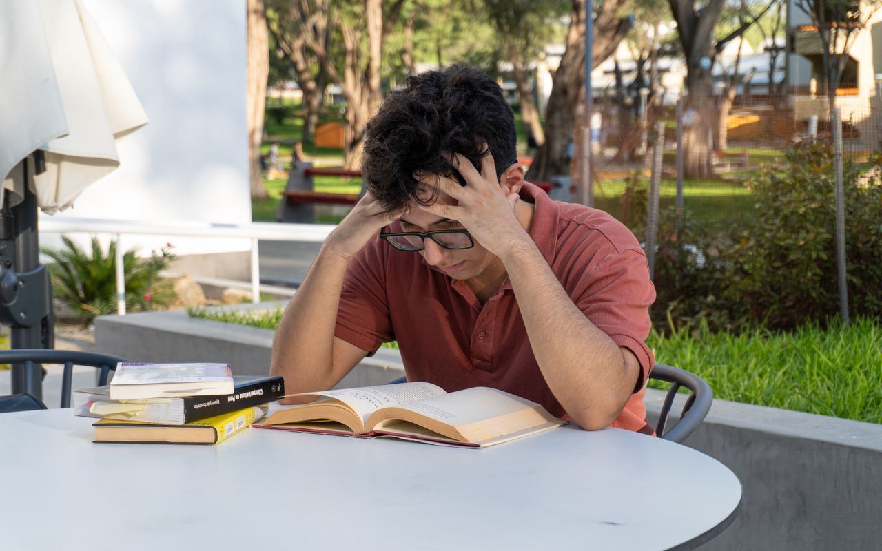 Anxious young man holding his head with books in front of him