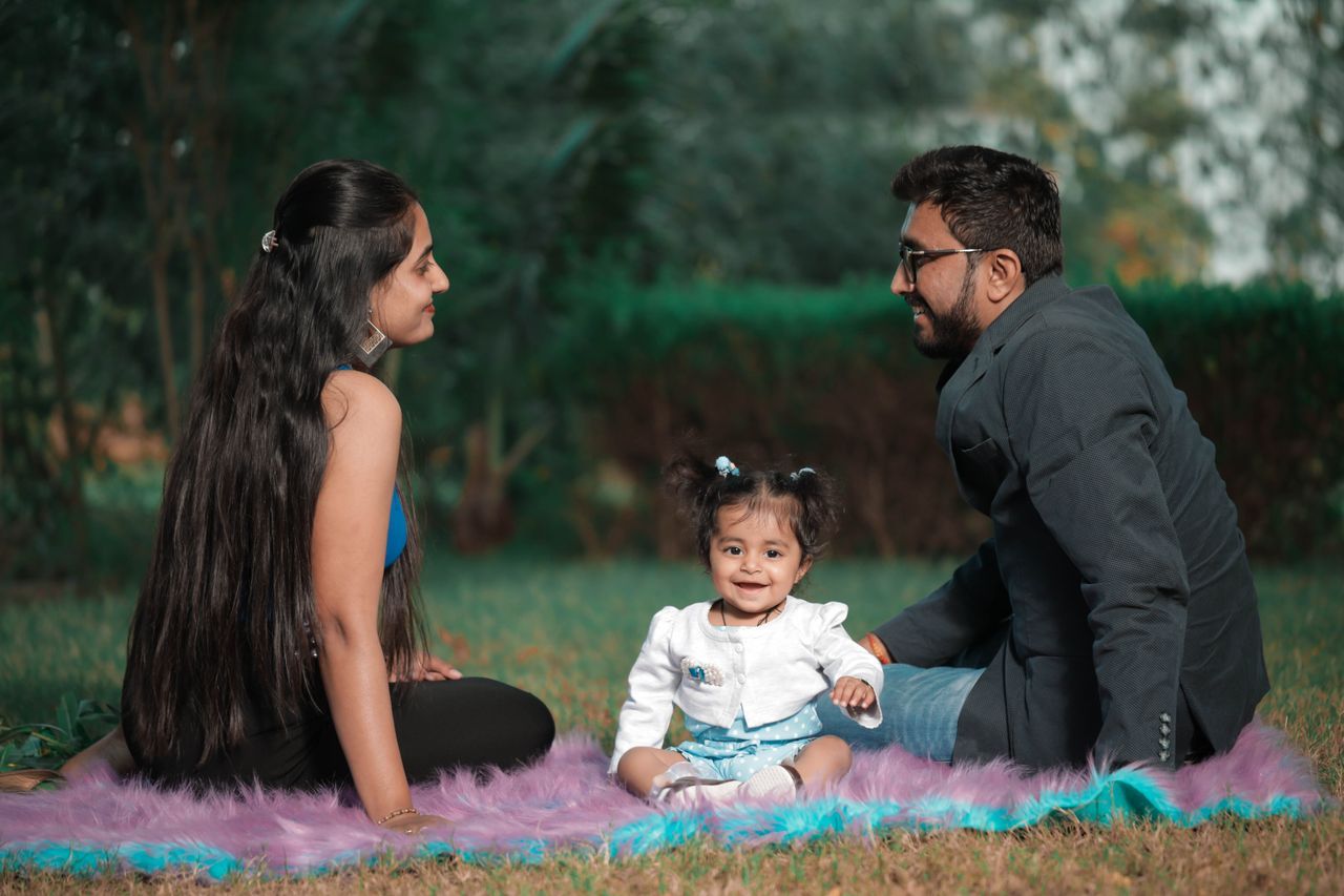 Newcomer family - Huband, wife & their baby sitting on a blanket in a park setting